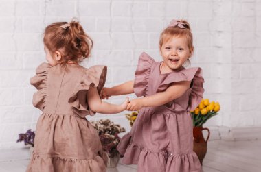 İki güzel kız dans edip çiçeklerle bir odada oynuyorlar.