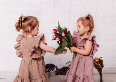 Çiçeklerle dolu bir odada oynayan iki güzel kız.