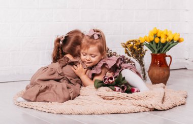 Çiçeklerle dolu bir odada sarılan iki güzel kız.