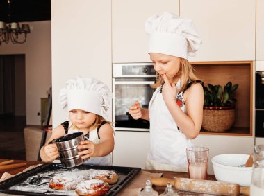Küçük kızlar mutfakta beyaz aşçı şapkalarıyla şeker tadarlar.