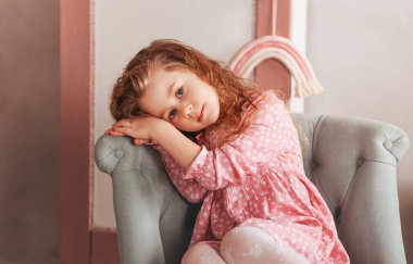 Çocuk odasında sandalyede oturan üzgün bir kız..