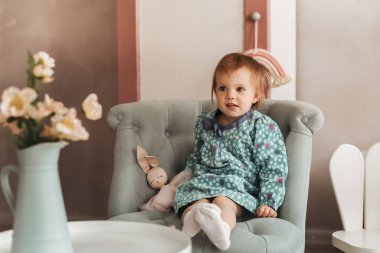 Küçük tatlı kız Todler çocuk odasında bir sandalyede oturuyor.