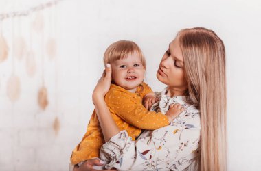 Güzel genç bir kadın, güzel kızı Todler 'ı kollarında parlak bir arka planda tutuyor.