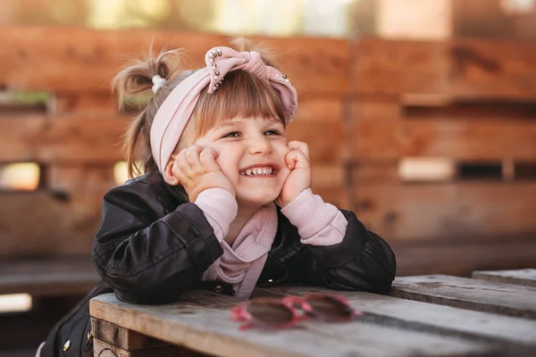 Little girl laughs and has fun on a bench in a summer cafe