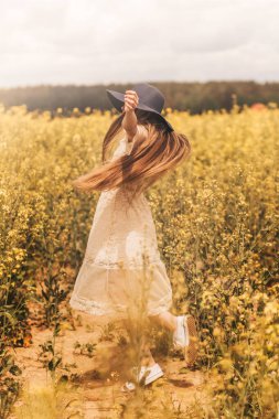 Genç ve mutlu bir kız çiçek açan kanola tarlasında doğanın tadını çıkarıyor. Gençlik ve özgürlük kavramı. Dikey