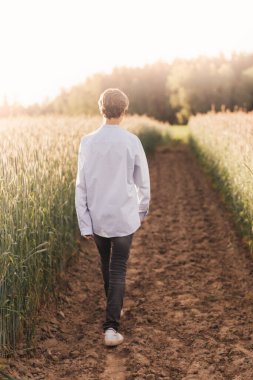 Genç bir adam yazın sahada yürür. Arkadan bak.
