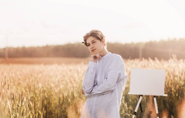 Genç adam yazın tuvalde resim yapıyor. Doğada sanatsal işler. Plein hava.