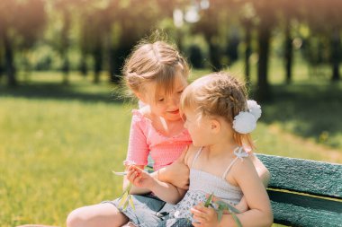 İki kız kardeş bankta oturuyor ve konuşuyor.