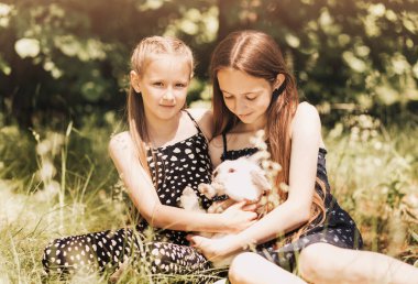 Parkta beyaz bir tavşanla oynayan iki kız. Çocuklar için bahar eğlencesi aktivitesi. Paskalya zamanı