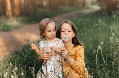 İki tatlı kız kardeş yazın doğada karahindiba ile oynuyorlar.
