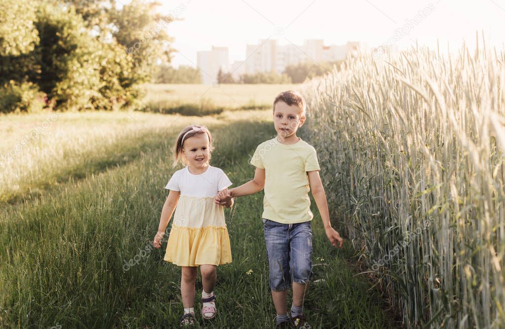 A boy and girl brother and sister play in the field in the summer. Happy summer vacation. Boy and girl on country road. Wheat field