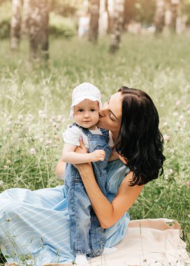 Genç bir anne parkta çimlerin üzerinde küçük kızıyla oynuyor.