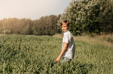 Okul çağındaki bir çocuk yeşil bir tarlada yürüyor. Yaz konsepti