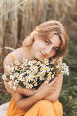 Genç ve güzel bir kız buğday tarlasında oturur ve elinde bir buket papatya tutar..