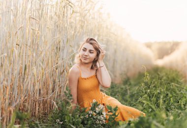 Genç ve güzel bir kız buğday tarlasında oturur ve elinde bir buket papatya tutar..