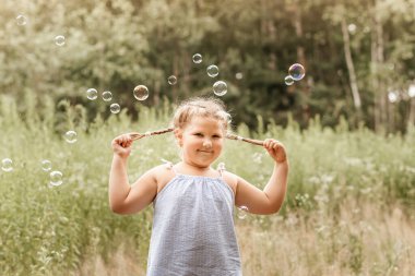Küçük kız yazın parkta sabun köpüğüyle oynuyor.