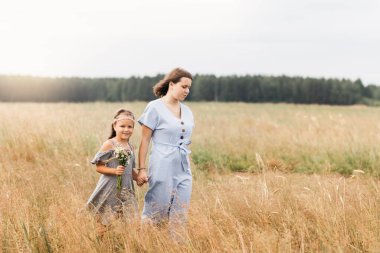 İki kız kardeş bir buket çiçekle çayırda yürüyor.