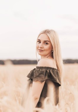 Genç, güzel, sarışın bir kadın yazın buğday tarlasında yürüyor.