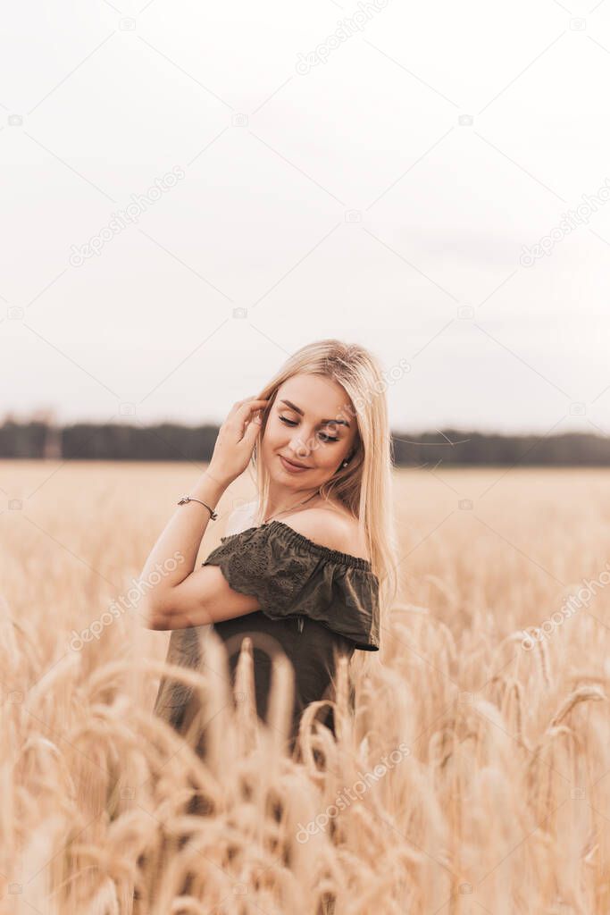 A young beautiful blonde woman with long hair walks through a wheat field in the summer