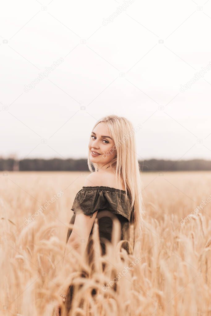 A young beautiful blonde woman with long hair walks through a wheat field in the summer