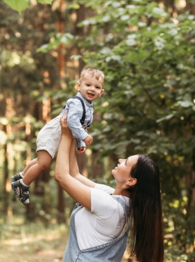 Genç mutlu anne yazın doğada küçük oğlunu kollarına alır. Anne ve çocuk sevgisi. Aile, doğa parkında günün tadını çıkarır.