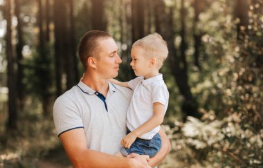 Genç bir baba, küçük oğlunu kollarına alır ve doğadaki başıboşlara bakar..