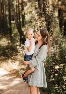 Genç ve güzel bir anne küçük oğlunu kollarına alır ve yazın doğada onunla oynar..