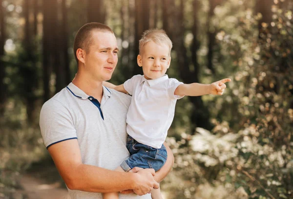 Genç bir baba, küçük oğlunu kollarına alır ve doğadaki başıboşlara bakar..