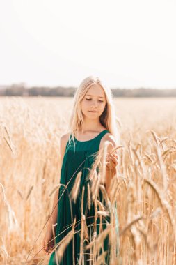 Güneşli bir günde, buğday tarlasında yürüyen uzun beyaz saçlı güzel bir genç kız.