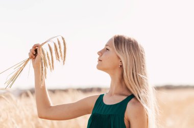 Güneşli bir günde, buğday tarlasında yürüyen uzun beyaz saçlı güzel bir genç kız.