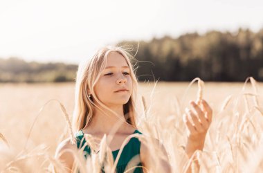 Güneşli bir günde, buğday tarlasında yürüyen uzun beyaz saçlı güzel bir genç kız.