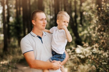 Genç bir baba, küçük oğlunu kollarına alır ve doğadaki başıboşlara bakar..