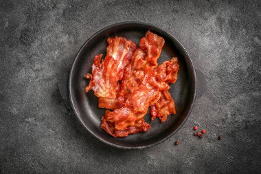 Siyah arka planda tavada kızarmış pastırma dilimleri. Üst görünüm.