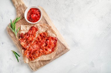 Kızarmış domuz pastırması, biberiye filizi ve domates sosu küçük kasede beyaz arka planda..