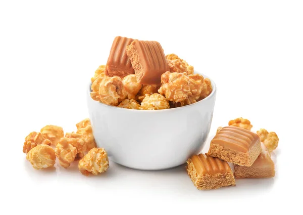 Sweet caramel popcorn and caramel candies in small bowl isolated on white background.