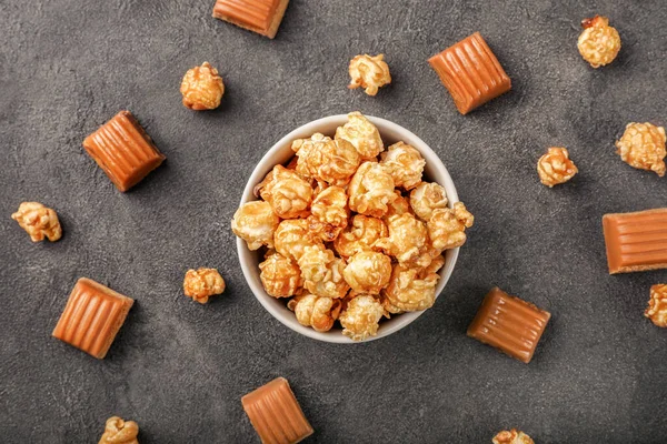 Sweet caramel popcorn in small bowl with caramel candies on dark background. Top view.