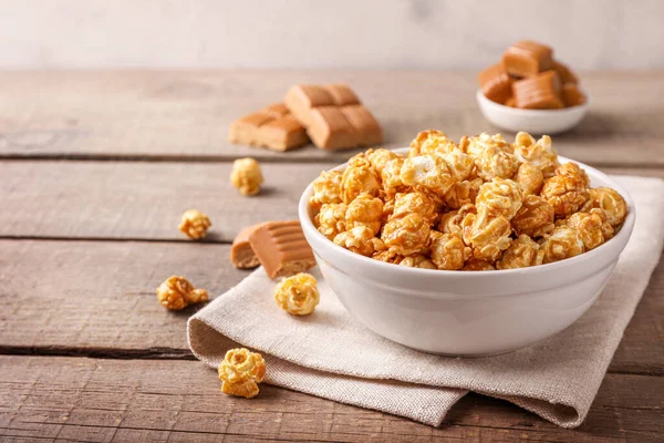 Sweet caramel popcorn and caramel candies on wooden background.