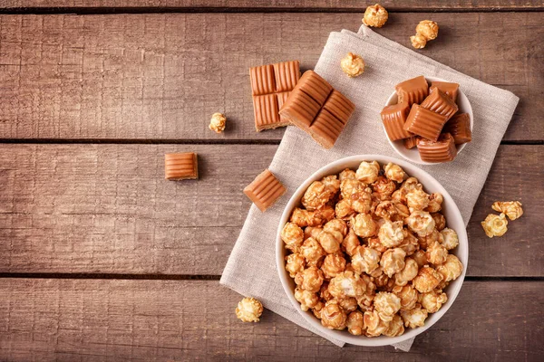 Sweet caramel popcorn and caramel candies on wooden background. Top view. Copy space.