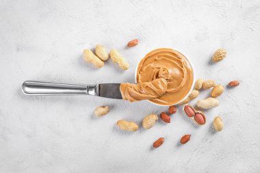 Küçük kasede kremalı fıstık ezmesi ve beyaz arka planda fıstık ezmeli bıçak. Üst görünüm.
