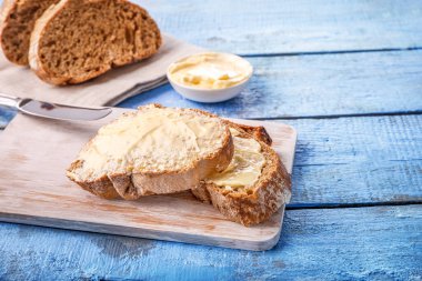 Mavi ahşap zemin üzerinde tereyağlı ekmek dilimleri.