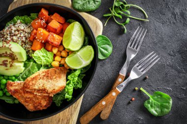 Kinoa, avokado, terli patates, kızarmış tavuk ve koyu arkaplanlı baharatla nefis bir öğle yemeği. Üst görünüm.
