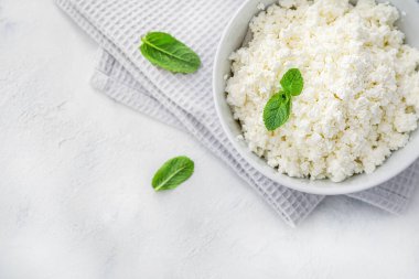 Beyaz arka planda mutfak peçetesi üzerine beyaz kâse içinde nane yaprakları olan taze süzme peynir. Üst görünüm.