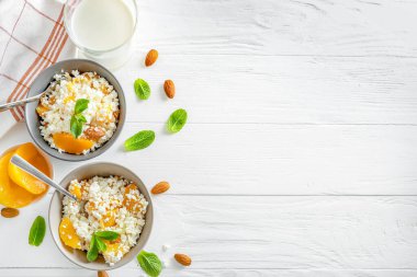 Nane yapraklı, şeftali parçalı ve beyaz ahşap arka planda badem fıstıklı taze süzme peynir. Üst Manzara. Boşluğu kopyala.