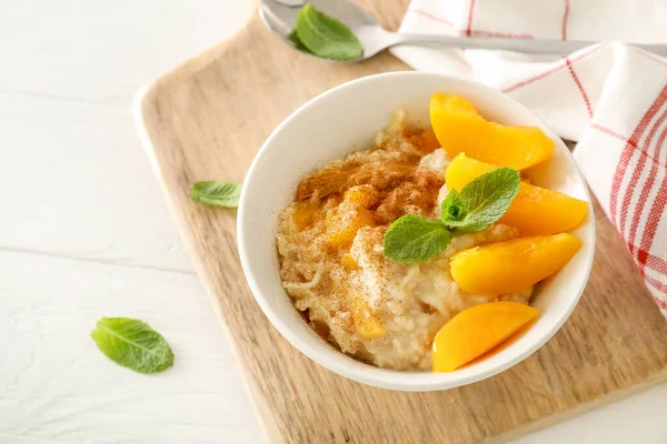 Nane yapraklı yulaf ezmesi kasesi, tarçın ve şeftali parçaları beyaz arka planda tahta kesme tahtasında..