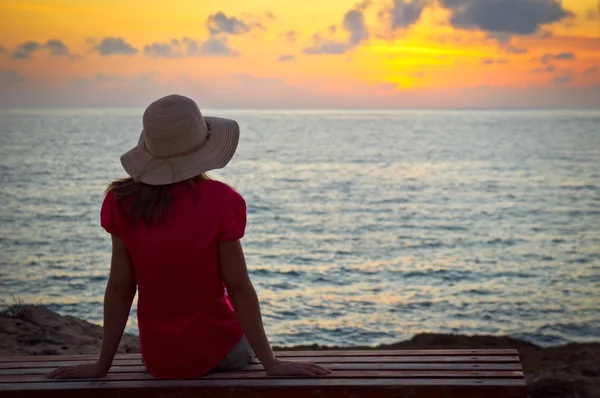 Jovem mulher de chapéu sentada e olhando para o pôr do sol — Fotografia de Stock