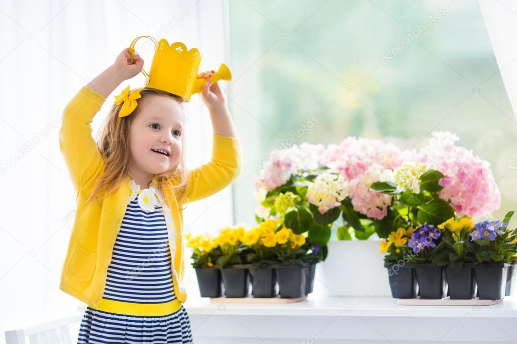 Little girl watering blooming flowers at home