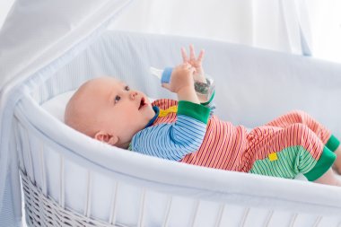Little baby with bottle in white bed