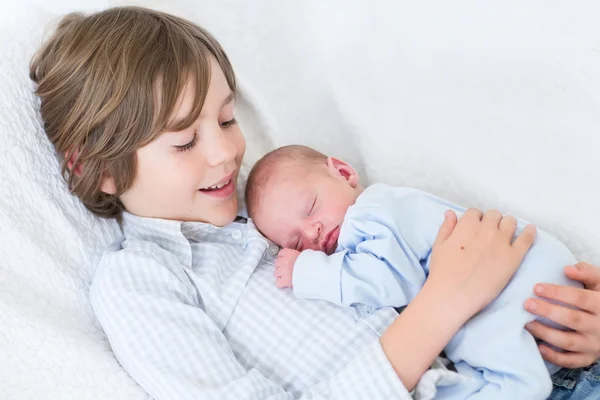 Glücklich lachender Junge hält seinen schlafenden neugeborenen Bruder — Stockfoto