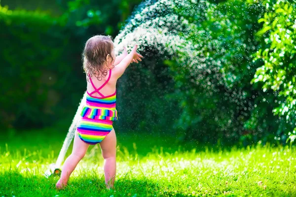 Маленькая девочка играет с садовым дождевателем — стоковое фото