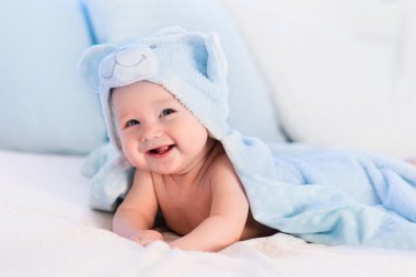 Baby boy in blue towel on white bed clipart